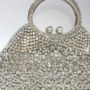 Détail d'une pochette argentée à strass avec poignée en métal et fermoir perle