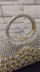 Détail de pochette en métal doré avec strass, fermoir perle et poignée anneau