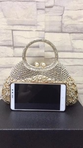 Détail de la pochette en strass montrant la taille par rapport à un smartphone sur socle
