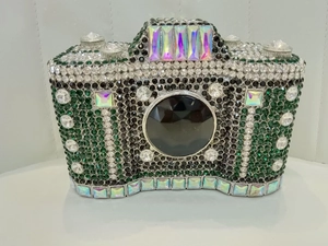 Detailed view of luxury camera-shaped clutch bag with emerald and black rhinestones