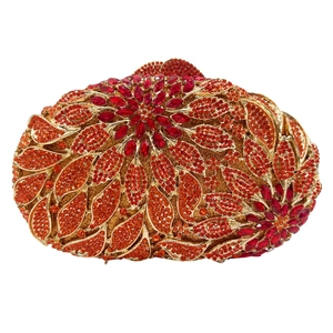 Macro detail of luxury leaf-patterned clutch with red and orange crystals on gold metal