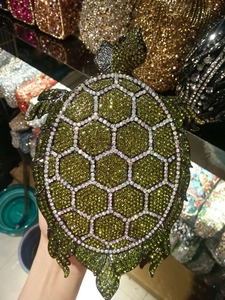 Detail of creative turtle-shaped evening clutch bag with green and white crystals