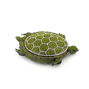 Exquisite turtle-shaped clutch bag encrusted with green and white crystals on white backdrop