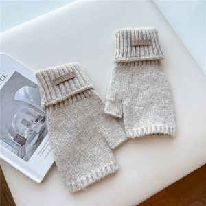 Close-up of beige cable knit fingerless gloves with a leather logo patch on white fabric