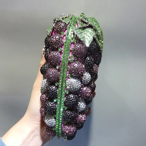 Close-up of a grape-shaped clutch bag with purple and green crystals held in hand