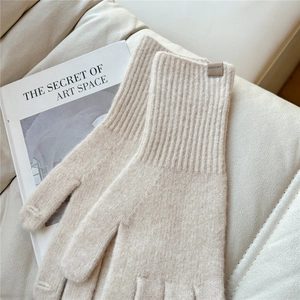 Detailed texture of beige knit gloves featuring a ribbed cuff and leather brand label