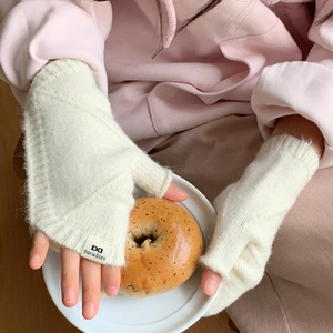 Détail de gants sans doigts en grosse maille blanche avec texture mohair et étiquette de marque