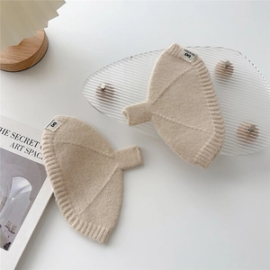 Détail de gants en tricot crème avec bord côte et étiquette sur fond minimaliste