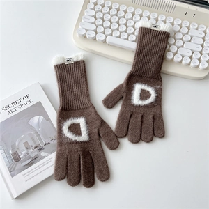 Détail de gants en tricot marron avec écusson lettre D et revers en fausse fourrure blanche