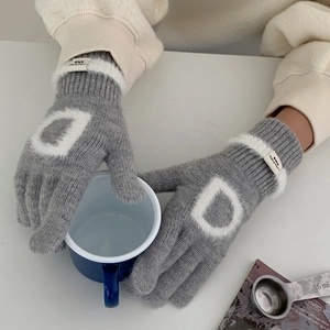 Détail d'un gant en tricot gris avec motif D blanc et bordure en fausse fourrure douce