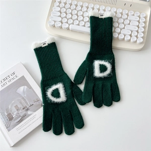 Détail de gants en tricot vert foncé avec lettre D en peluche et bordure en fausse fourrure