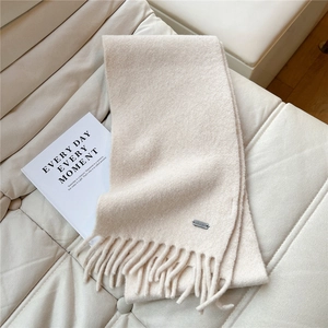 Détail d'une écharpe en maille blanc crème avec franges et plaque logo argentée