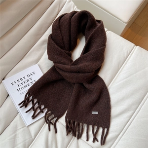 Détail d'une écharpe en tricot marron foncé avec texture épaisse, franges et logo argenté