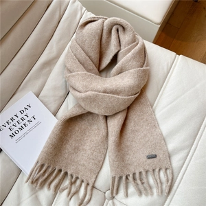 Détail d'une écharpe en maille beige avec de longs pompons et plaque logo sur cuir blanc