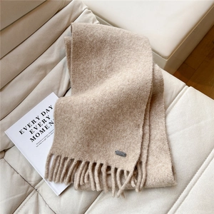 Détail de l'écharpe en maille beige avec pompons et plaque métallique sur un canapé