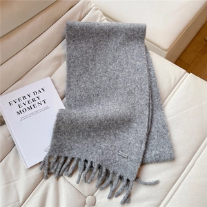 Détail de l'écharpe gris foncé avec texture laineuse, franges et petit logo métallique