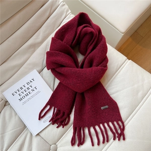 Détail d'une écharpe en maille bordeaux avec franges et étiquette argentée sur cuir doux