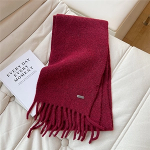 Gros plan sur l'écharpe en tricot bordeaux avec glands et logo métallique sur un canapé