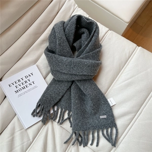 Gros plan d'une écharpe en maille gris foncé avec pompons et étiquette de marque en métal