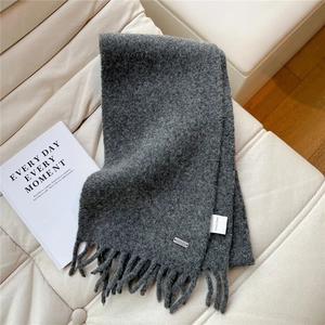 Détail de la texture d'une écharpe à franges gris foncé avec logo métallique chic