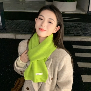Detail of neon green ribbed knit scarf with cashmere label on beige coat background
