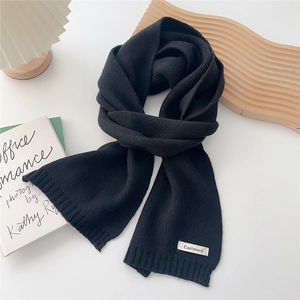 Detail of soft black cashmere knit scarf with minimalist fabric label on white background