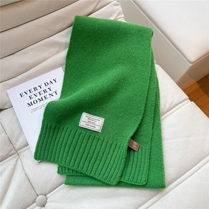 Detail eines grünen Strickschals aus Wolle mit Etiketten auf einem beigen Ledersofa
