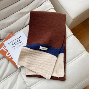 Detail of tricolor chunky knit scarf with woven label on a soft textured surface