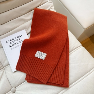 Detail eines Schals aus 100% Wolle in gebranntem Orange mit Rippstrickkanten und Etikett