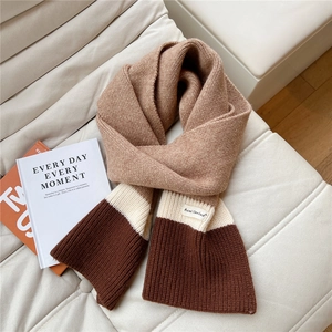 Detail of three-tone knitted scarf showing soft texture and brand label on a sofa