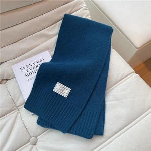 Nahaufnahme des pfauenblauen Strickschals aus 100% Wolle mit Etikett auf Ledersofa