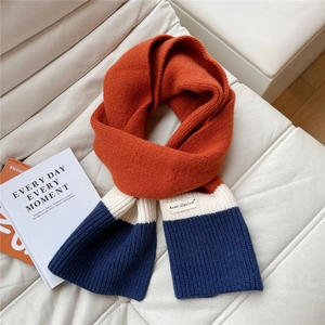 Close-up of tricolor knit scarf showing orange, beige, and navy texture with woven tag