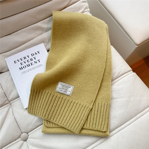 Detail eines senfgelben Schals aus 100% Wolle mit Textur und Marken-Stoffetikett