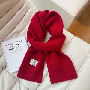 Detail eines roten Strickschals aus 100% Wolle mit Rippenrand auf weißem Leder
