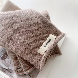 Close-up of oatmeal wool gloves with a 100% wool label showing thick knit texture