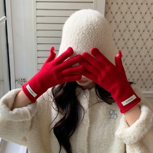 Detail of red wool knit gloves with white logo tag and plush white beanie hat