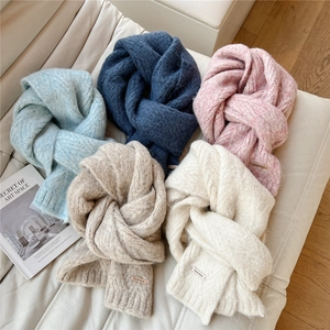 Macro shot of thick cable knit scarves in pastel colors with golden metal logo brand details