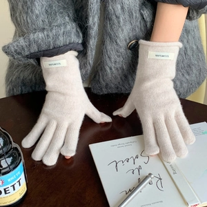 Detail of off-white knitted wool gloves with 100% wool label and folded ribbed cuffs