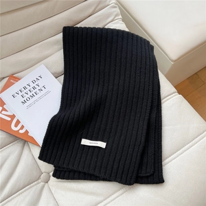Detail of 100% pure wool black knit scarf featuring vertical ribbing and minimalist white label