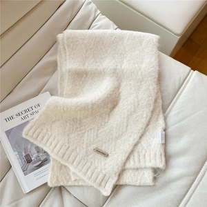 Detail of soft cream knitted scarf with a textured metal logo plate and wash label tag