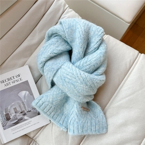 Close-up of light blue chunky knit scarf texture with a brown leather logo label on a sofa