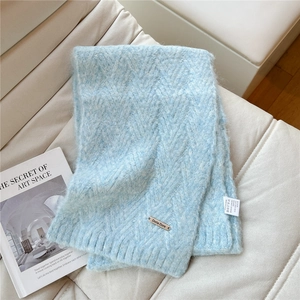 Detail of light blue knit scarf showing V-shaped chevron texture and metal brand tag