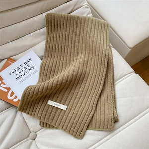 Detail of khaki 100% wool knitted scarf showing ribbed texture on a white sofa