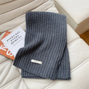 Detail of dark gray ribbed knit scarf in 100% wool on a soft cream textured sofa