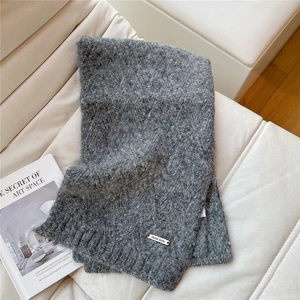 Detail of grey knitted scarf with Doria Dore metal logo on a quilted background