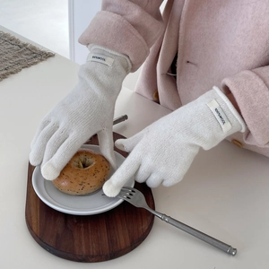 Detailed view of white knit wool gloves featuring the 100% wool label on the wrist cuff