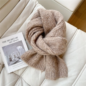Close-up of thick cable knit texture and brown leather label on light brown scarf