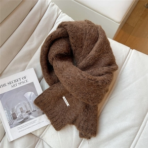 Detail of soft brown knitted scarf with metal logo plate on white textured fabric