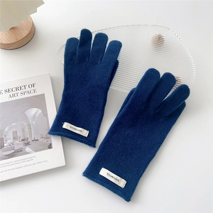 Detailed view of dark blue 100% wool knitted gloves with premium woven label on white table
