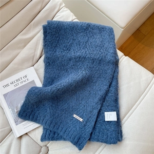 Detail of blue knit scarf showing soft alpaca texture and metallic logo on white sofa